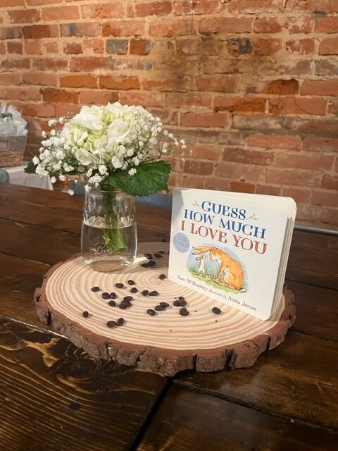 white flowers in jar beside "guess how much I love you" book & on top of piece of tree stump