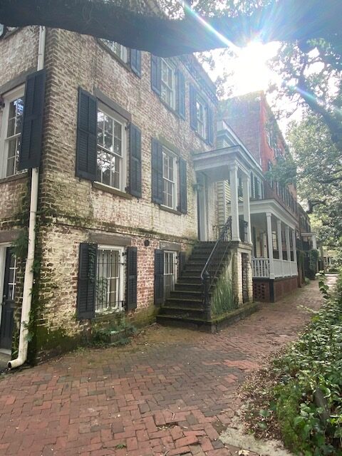 older brick house on brick path with moss growing along staircase leading to front door